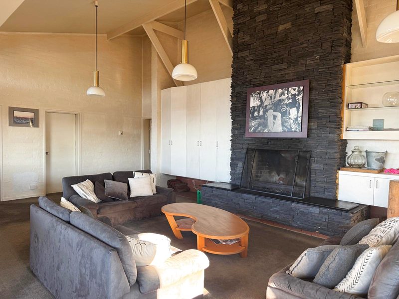 The top-level living room: sofas around a low table facing a tall dark-stone chimney breast and open fire, under a raked timber-framed ceiling.